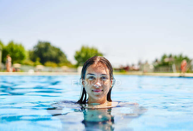 Glückliches Weibchen mit nassen Haaren schwimmt im sauberen Poolwasser, während sie an sonnigen Sommertagen in die Kamera blickt — Stockfoto