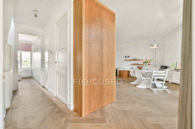 Corridoio che conduce alla spaziosa sala da pranzo con sedie bianche e tavolo rotondo in moderno appartamento leggero con pavimento in legno e design minimalista — Foto stock