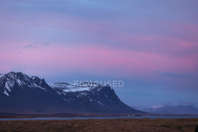 Malerische Landschaft aus felsigen Bergen mit schneebedeckten Gipfeln am Meer gegen den atemberaubenden rosafarbenen Himmel bei Sonnenuntergang in Island — Stockfoto
