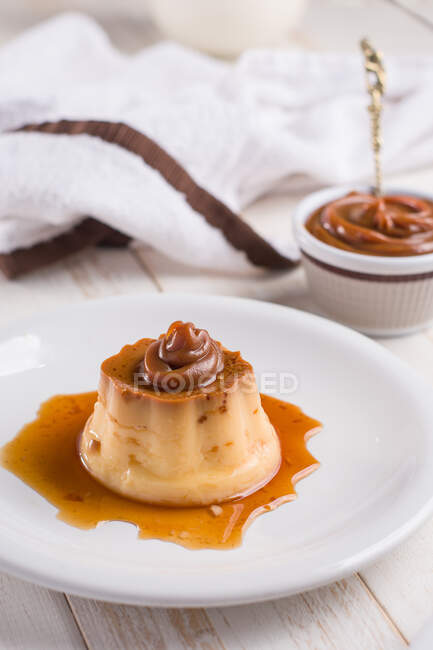 From above of egg custards topped with sweet Dulce de leche served on white plate on table with cutlery in kitchen — Stock Photo