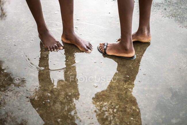 From above of crop unrecognizable black barefoot people standing in small puddle on asphalt road on street on So Tom and Prncipe island in daylight — Stock Photo