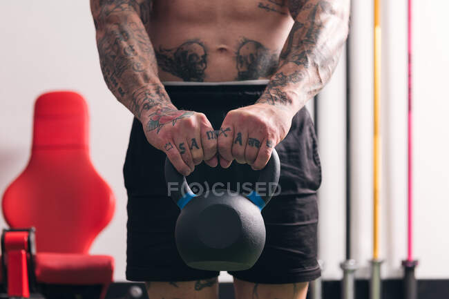 Kraftvoller hemdloser Bodybuilder mit Tätowierungen beim Training mit schwerer Kettlebell während des Functional Trainings im Fitnessstudio — Stockfoto