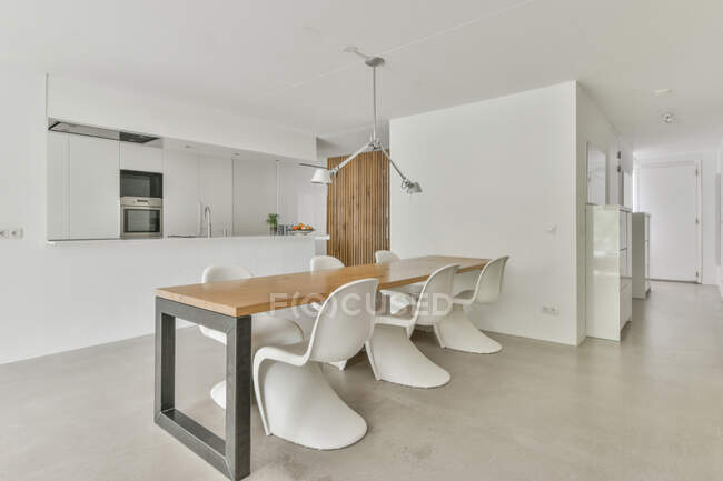 Современная столовая и кухонный интерьер со встроенной электротехникой против стола со стульями в доме — стоковое фото