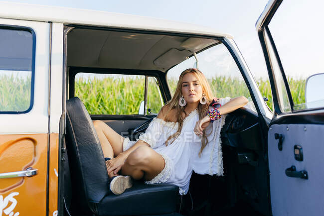 Симпатична блондинка сидить всередині старовинного фургона і спирається на панель приладів в сонячний день — стокове фото