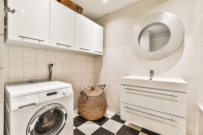 Interior do banheiro contemporâneo com máquina de lavar roupa e lavatório contra parede cerâmica com armário em casa — Fotografia de Stock