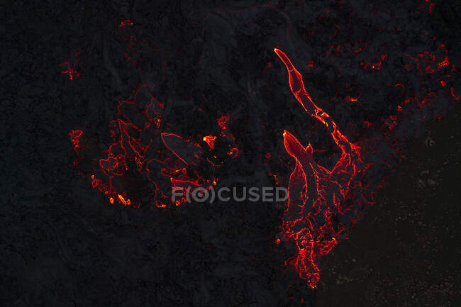 Vue de dessus du magma rouge chaud qui coule sur une surface montagneuse sombre la nuit dans les hautes terres d'Islande dans l'obscurité — Photo de stock
