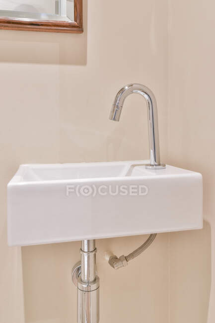 Белая керамическая раковина с блестящим хромированным краном установлена на бежевой стене в туалете — стоковое фото