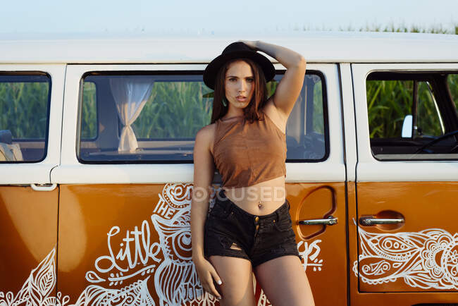 Attractive brunette girl with hat outside a van looking at the camera on a sunny day — Stock Photo