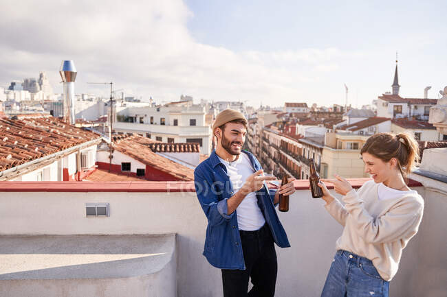 Full body of cheerful friends raising bottles of beer while laughing on balcony in old city — Stock Photo