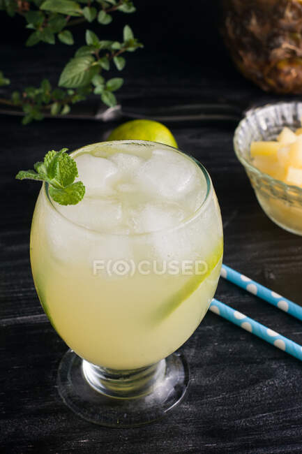 From above of cold cocktail consisting of lime piece ice cubed and mint leaf served with bowl of chopped pineapple — Stock Photo