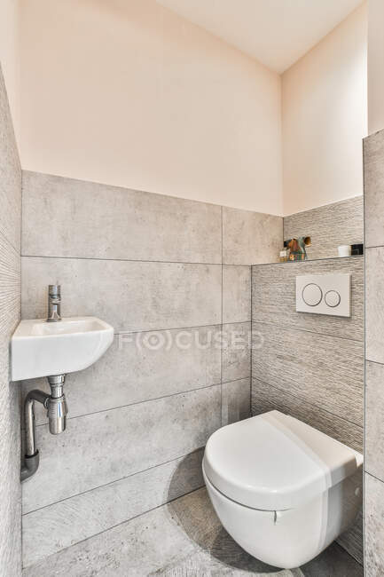 Интерьер современной ванной комнаты с унитазом и умывальником на серой черепичной стене в светлом доме — стоковое фото