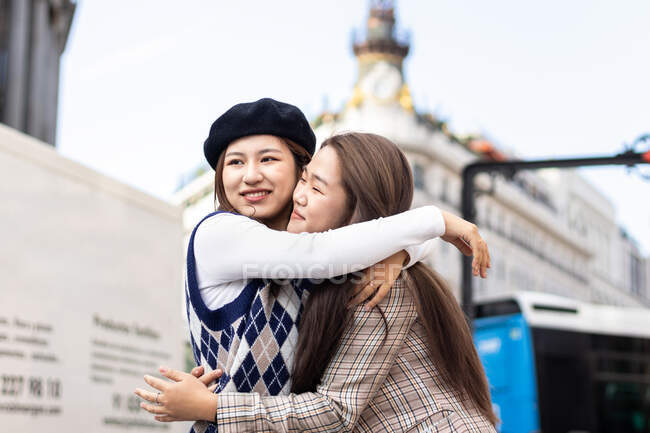 Seitenansicht lächelnder ethnischer Freundinnen, die sich umarmen, während sie in der Nähe einer Straße in Madrid während des gemeinsamen Urlaubs stehen — Stockfoto