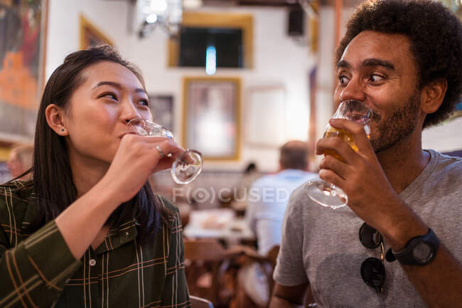 Foco suave de casais multirraciais bebendo bebidas enquanto jantam juntos no restaurante moderno durante o evento festivo — Fotografia de Stock