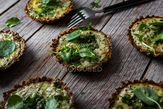 From above of cauliflower and walnut cakes with greens near fork on planked wooden table — Stock Photo