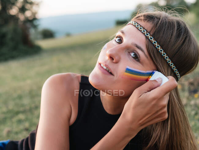 Primer plano de una mujer pintando un arco iris en su mejilla con un palo - foto de stock