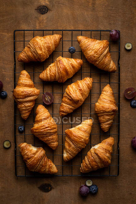 Dall'alto gustosi croissant dolci appena sfornati serviti con frutta posta su griglia metallica su tavolo di legno — Foto stock