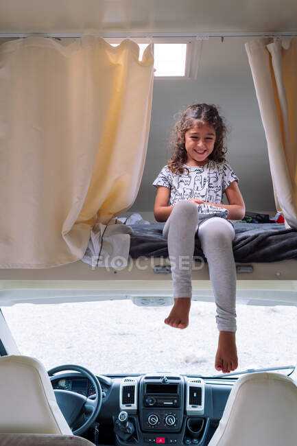 Smiling barefoot child in ornamental t shirt sitting on mattress in vehicle during trip in daytime — Stock Photo