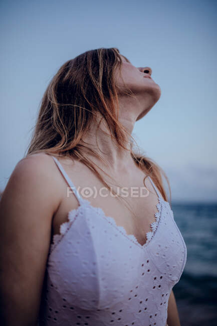 Приємна жінка з довгим волоссям у модному вбранні стоїть на березі моря увечері. — стокове фото