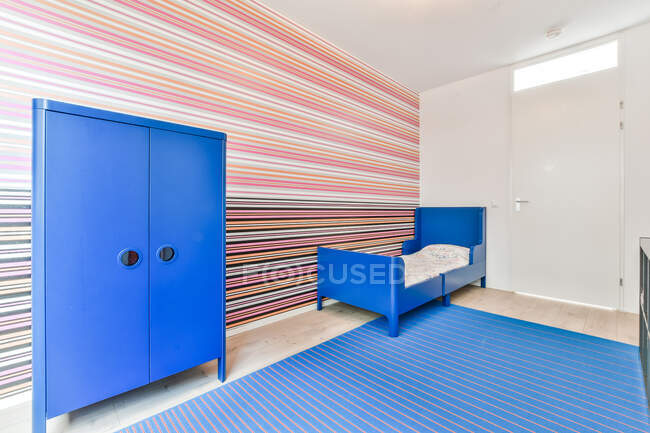 Креативный дизайн спальни с кроватью между аквагримом на столе и стеной с полосатым полом дома — стоковое фото