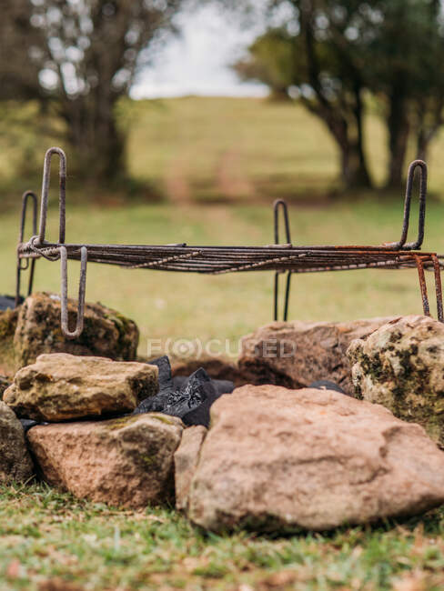 Grille métallique rouillée posée sur des pierres au-dessus du charbon sur un terrain herbeux au camping le jour — Photo de stock