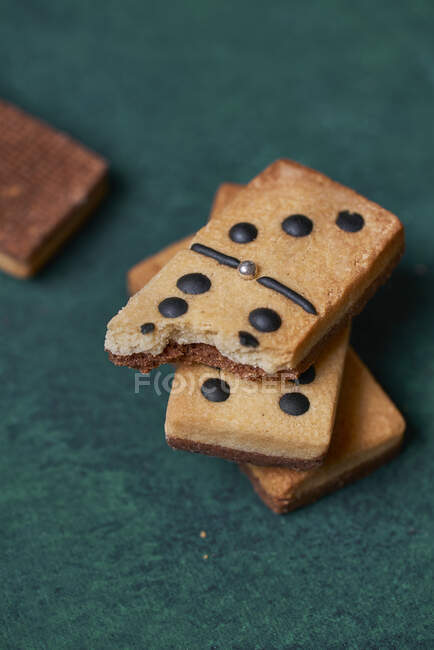 Heap de doces saborosos dominós crocantes em forma de biscoitos com pontos pretos e pedaço mordido espalhados na superfície verde na sala de luz — Fotografia de Stock