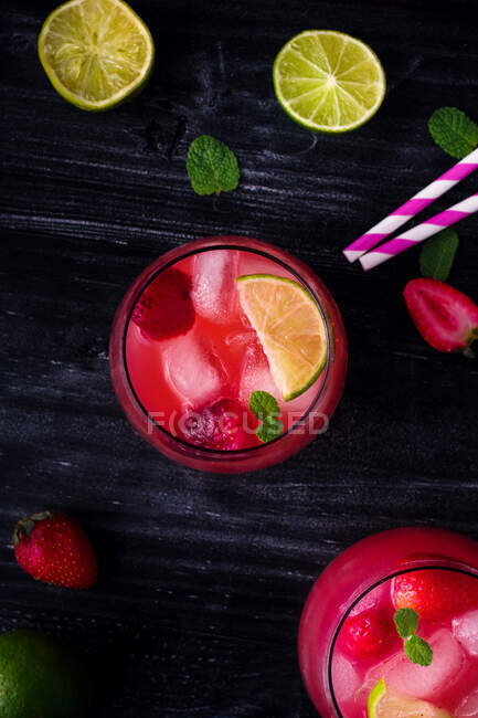 Du dessus de verre d'eau de coco froide avec des tranches de citron vert et des fraises servies sur une table en bois sombre — Photo de stock