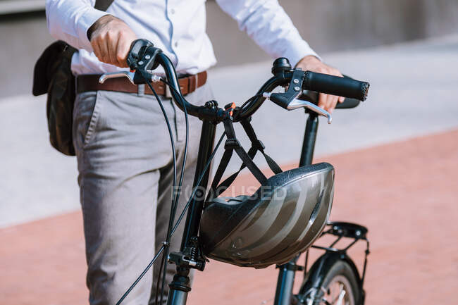 Cropped unrecognizable executive worker in formal wear standing with bicycle near modern office building — Stock Photo