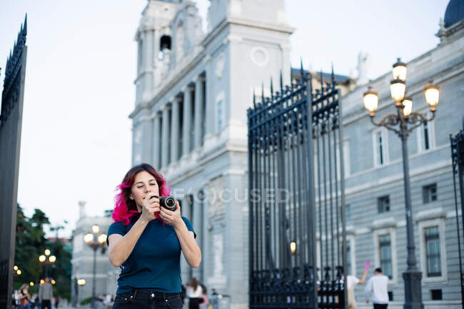 Viajante feminino focado tirando foto na câmera da foto enquanto estava na rua com luz de rua perto do edifício antigo com cerca na cidade — Fotografia de Stock
