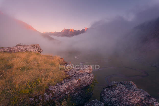 Terreno erboso circondato da aspre montagne nella natura della Spagna con tempo nebbioso all'alba — Foto stock