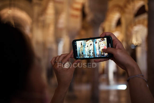 Vue latérale d'une voyageuse asiatique anonyme prenant des photos sur smartphone alors qu'elle se tenait debout dans une ancienne mosquée — Photo de stock