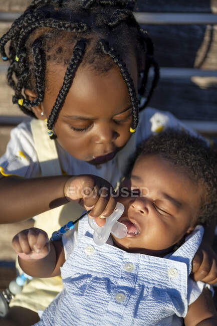 Зверху спокійна афроамериканська дівчина з чорними плесками, що дає пацифікатор сну немовляті в сонячний день. — стокове фото