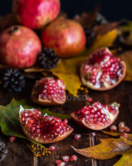 Partes de granada roja fresca colocadas sobre una mesa de madera oscura con hojas de otoño - foto de stock