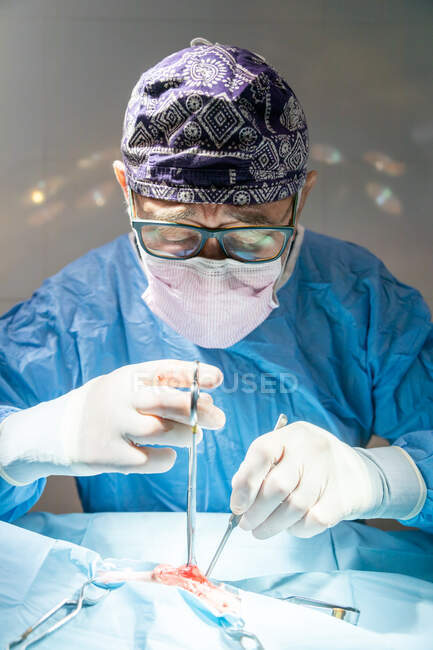 Chirurgien masculin senior professionnel en masque et uniforme faisant opération sous lampe dans la salle d'opération — Photo de stock