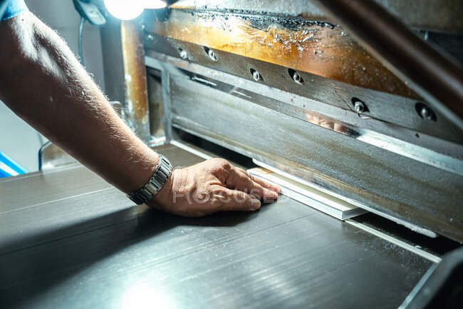 Ernte unkenntlich gealterten männlichen Handwerker setzen Papierblätter in Metalldruckmaschine mit glühender Lampe in Fabrik — Stockfoto
