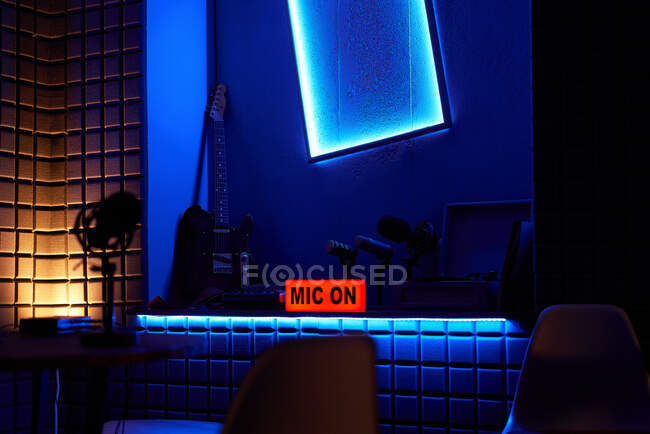 Современная темная студия с ярким неоновым освещением и вывеской Mic On на столе с различными музыкальными инструментами — стоковое фото