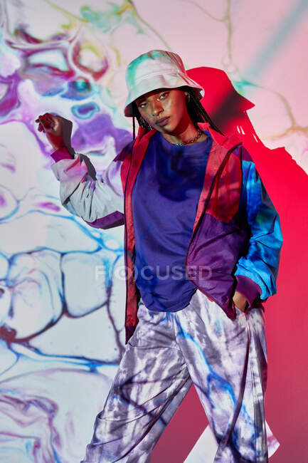 Junge dominikanische Teenagerin in modischem Outfit und Hut steht neben weißer Wand mit kreativen abstrakten Projektionen und blickt in die Kamera — Stockfoto