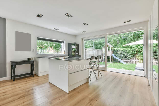 Kitchen counter with chairs placed in spacious dining room with window and doorway overlooking patio with grassy lawn and children slide — Stock Photo