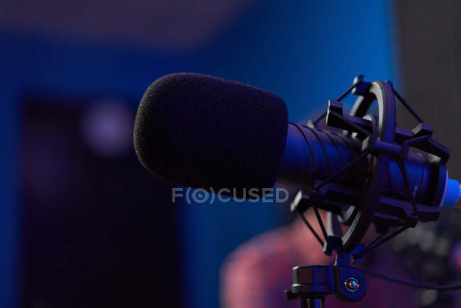 Microfone moderno em tripé colocado na mesa em estúdio escuro com iluminação de néon antes de gravar podcast — Fotografia de Stock