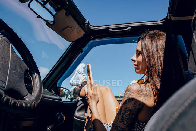 Seitenansicht einer jungen Frau, die auf dem Beifahrersitz im Auto sitzt und ihr Handy benutzt — Stockfoto