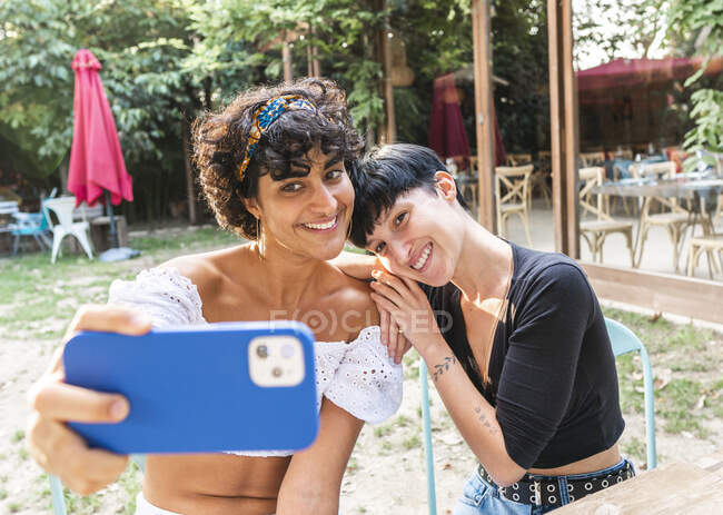 Conteúdo amigável multirracial fêmeas tomando auto tiro no telefone móvel enquanto desfrutam de fim de semana juntos no parque de verão — Fotografia de Stock