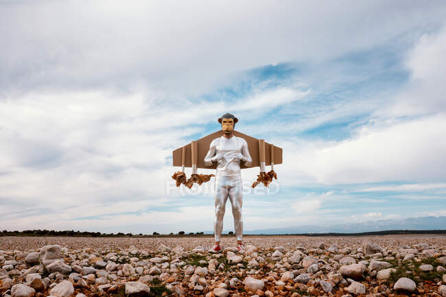 Мужчина в серебряном костюме и обезьянья маска, стоящая с реактивным ранцем на каменистой земле летом — стоковое фото