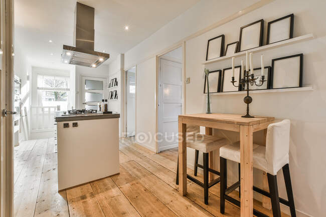 Moderne Küche mit Dunstabzugshaube über Gasherd gegen Gestelle auf Regalen über Kandelaber auf Holztisch im Leuchtturm — Stockfoto