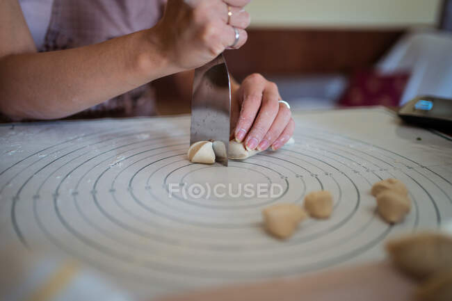 High angle of crop anonymous lady cutting raw dough with putty knife while preparing homemade dumplings sitting at table in kitchen — Stock Photo