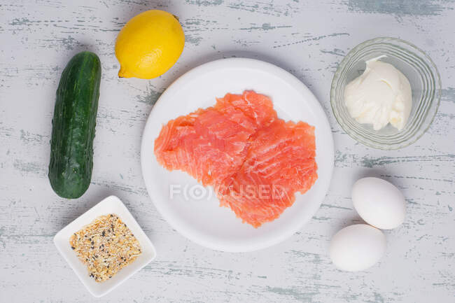 Вид сверху куска копченого филе лосося на тарелке, выставленной на стол с различными свежими ингредиентами — стоковое фото