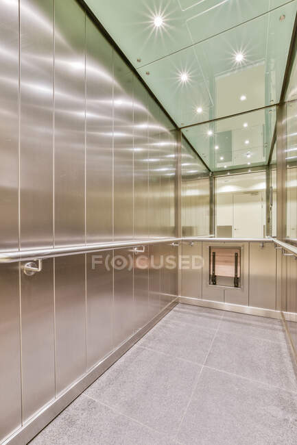 Interior of long lift cab with metal panels and railings with reflection of glowing lamps on ceiling in contemporary building — Stock Photo