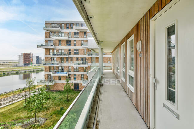Schmaler langer Balkon eines modernen Mehrfamilienhauses mit Blick auf die Flusspromenade und Grünfläche mit Bäumen und Sträuchern und das nächste Haus — Stockfoto