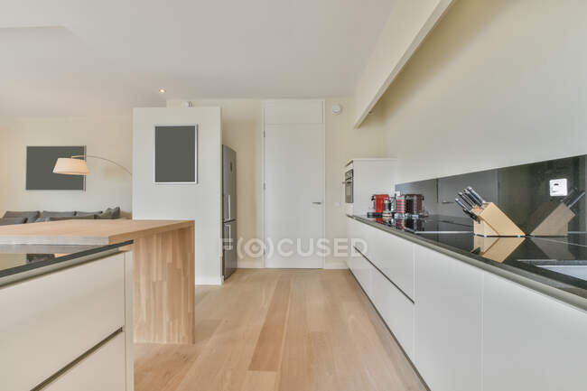 Armadi bianchi con attrezzature moderne e vari utensili sul bancone in spaziosa cucina con interni eleganti in appartamento leggero — Foto stock
