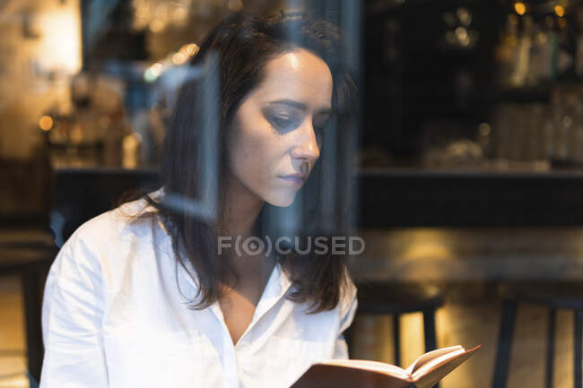 Через вікно сконцентрованої молодої жінки в білій сорочці, яка сиділа в кафе. — стокове фото