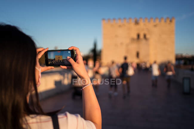 Crop viajante feminino anônimo tirar foto do edifício histórico no smartphone localizado na rua lotada na Espanha em fundo borrado — Fotografia de Stock