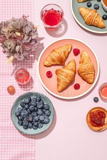 De cima da composição de chapeado com croissants doces cozidos no forno frescos servidos com bagas e engarrafamento colocados na mesa rosa — Fotografia de Stock